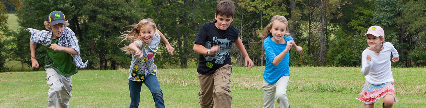 A group of kids dressed in John Deere clothing run through a field