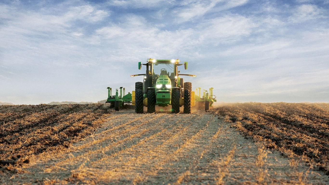 รถแทรกเตอร์ John Deere ขับเคลื่อนอัตโนมัติกำลังดึงอุปกรณ์เตรียมดินผ่านทุ่งโล่ง